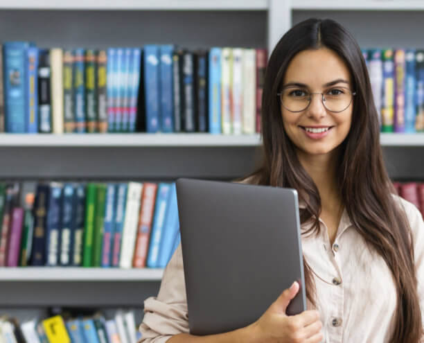 Student standing in library, holding a laptop