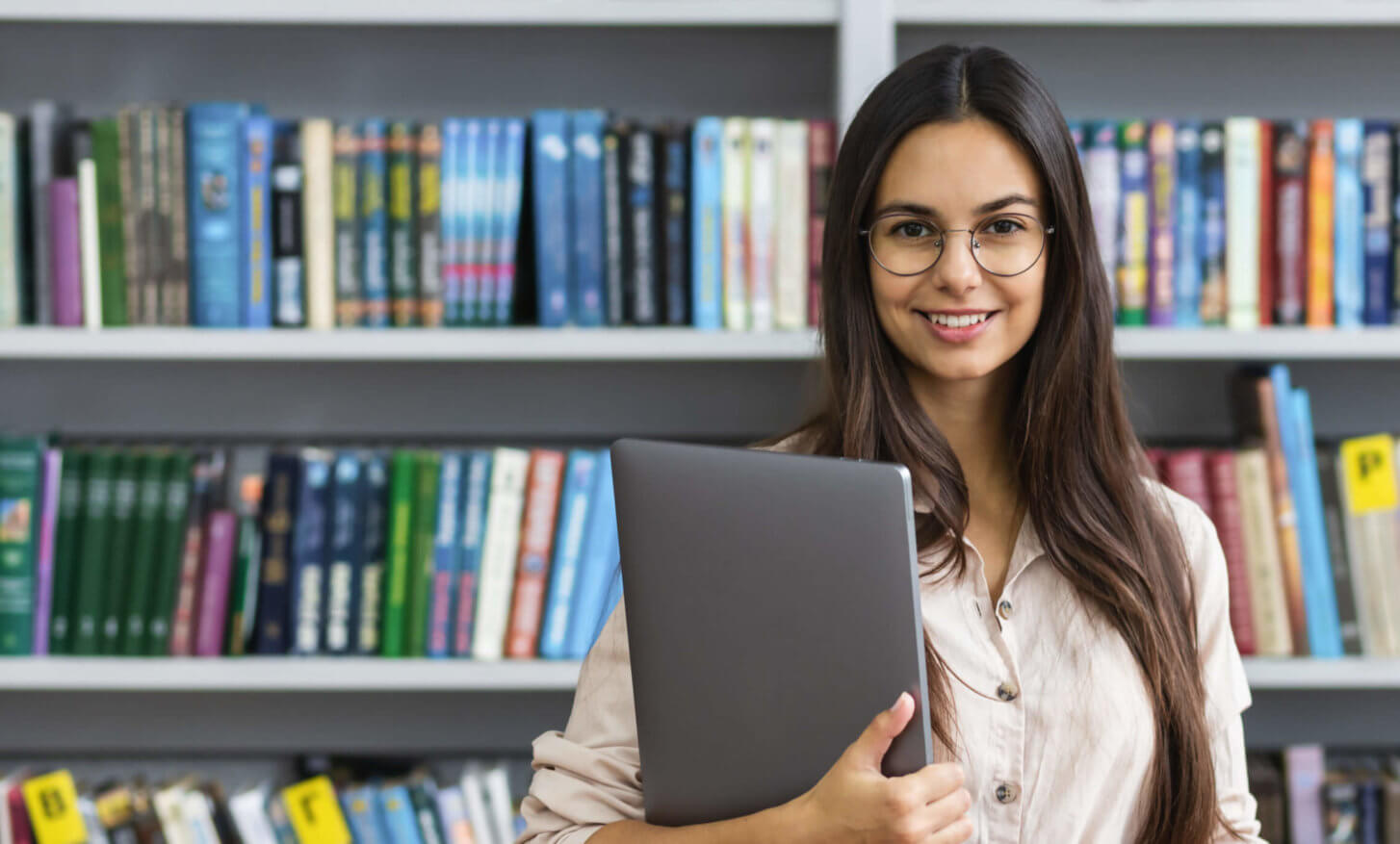 Student standing in library, holding a laptop