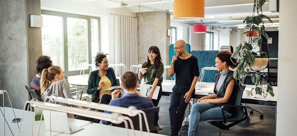 A group of people in a circle happily discuss something in the office.