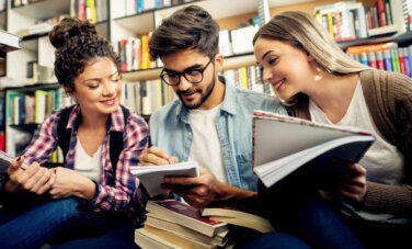 Three people happily discuss something at a library.