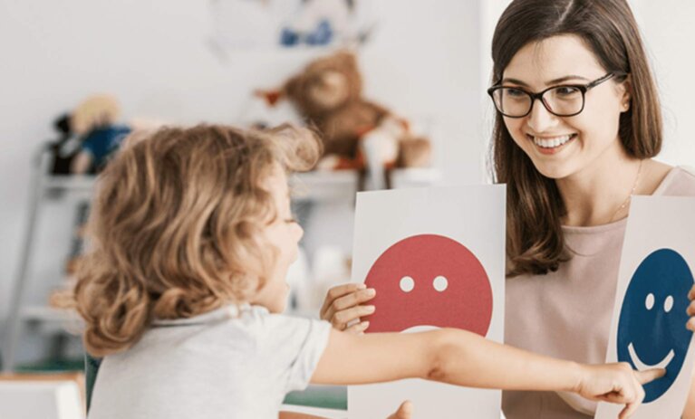 Graduate Certificate of Psychological Science Woman sits at desk holding two paper cards with an image on each. A young child sits in front of her and is pointing at one and speaking.