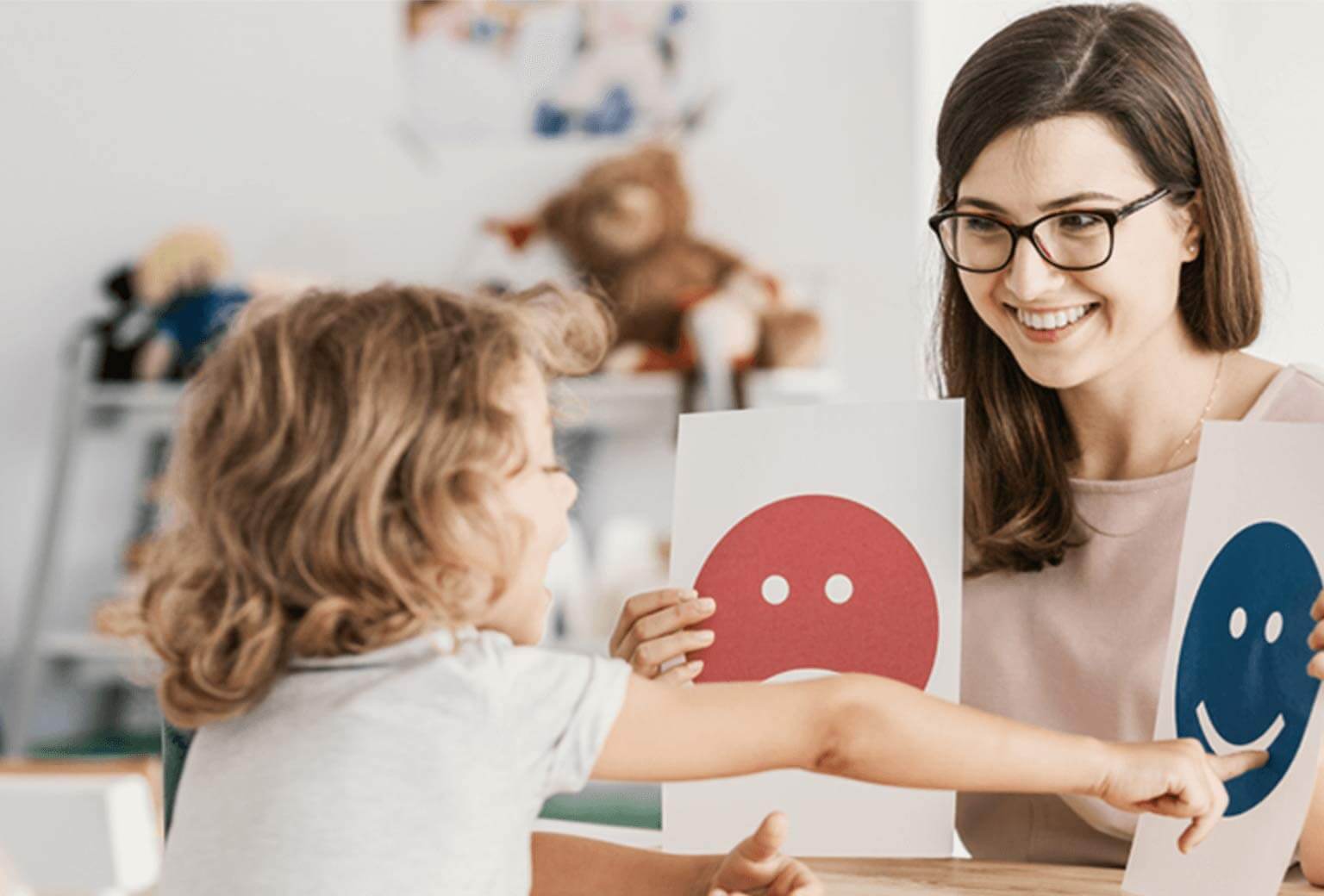 Graduate Certificate of Psychological Science Woman sits at desk holding two paper cards with an image on each. A young child sits in front of her and is pointing at one and speaking.