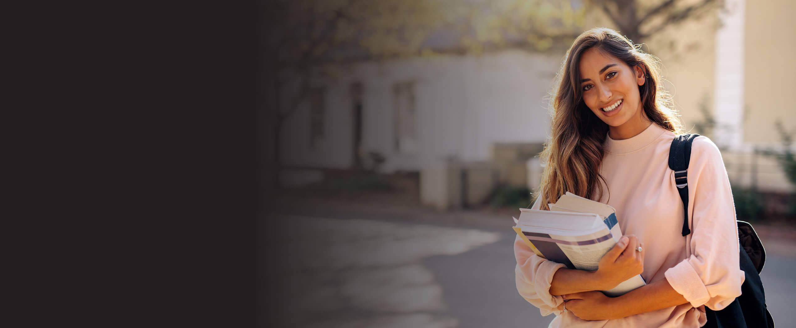 ACAP - 191020211224 - Experience ACAP - Landing Page Banners - Generic A student standing on campus with books in hand and smiling.
