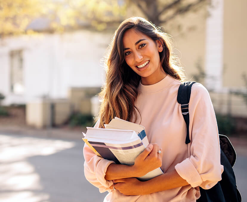 A student standing on campus with books in hand.