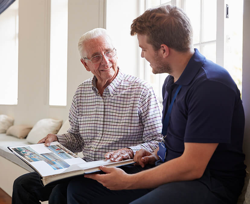 ACAP-191020211224-ExperienceACAP-LandingPageBannersMobile-Psychology A student sitting with a senior citizen and looking through a photo book.
