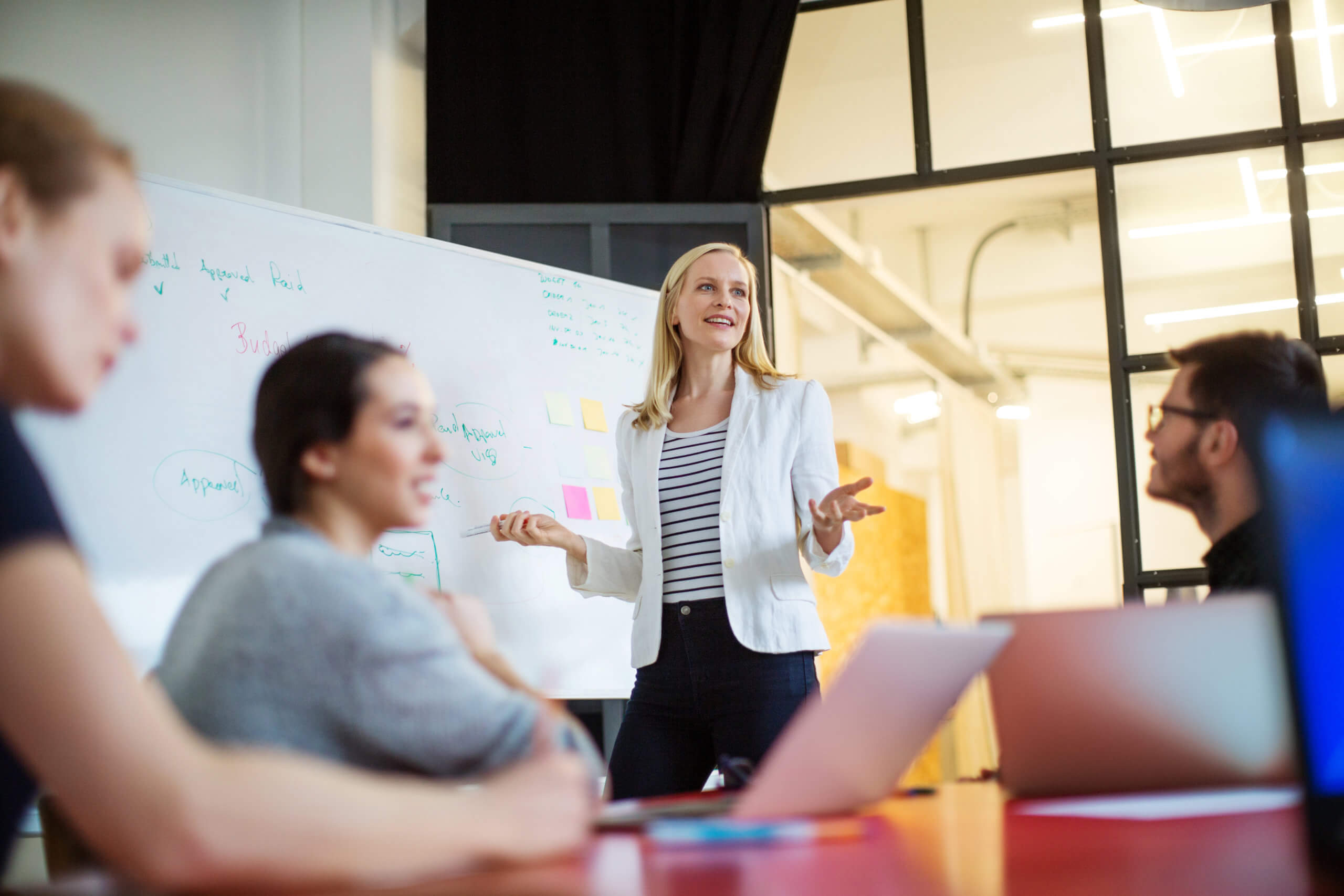 Businesswoman giving presentation on future plans to colleagues A woman leading a discussion with notes on a whiteboard.