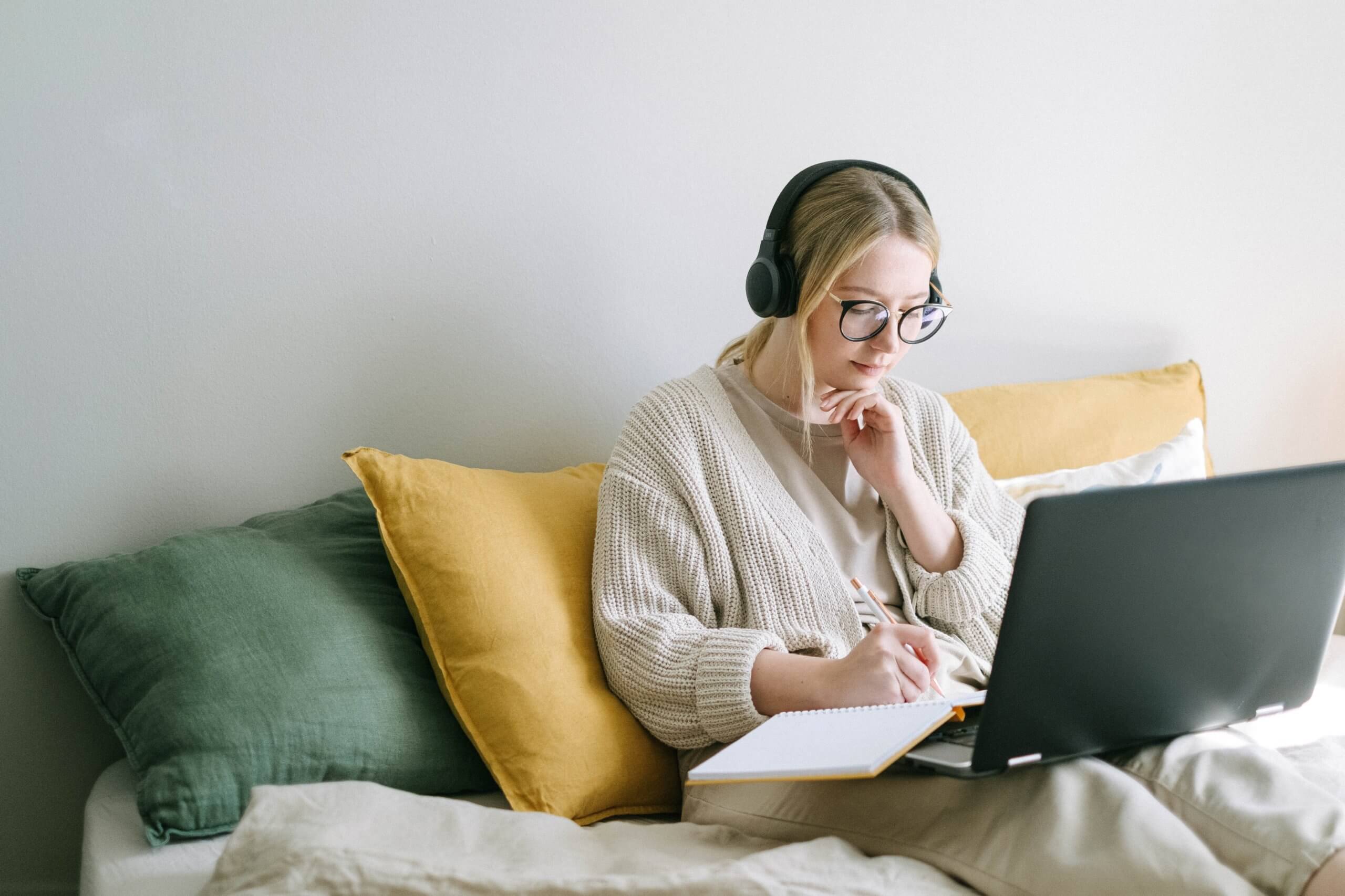 A woman sitting in bed with a laptop and headphones on.