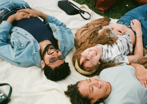 Three people laughing while lying on a picnic blanket