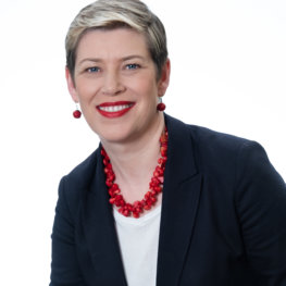 Woman wearing a red necklace and a blazer.