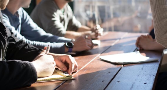 Group of people sitting at a desk with notepads.