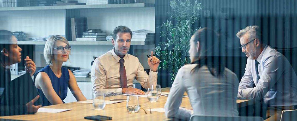 Coworkers communicating at desk seen through glass Group of work colleagues having a discussion at a desk.