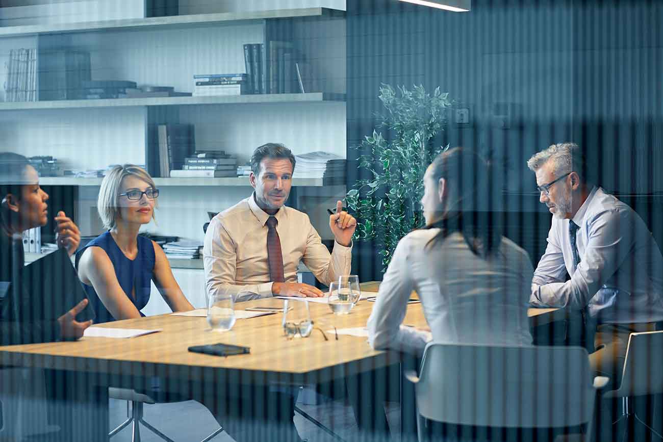 Coworkers communicating at desk seen through glass Group of work colleagues having a discussion at a desk.