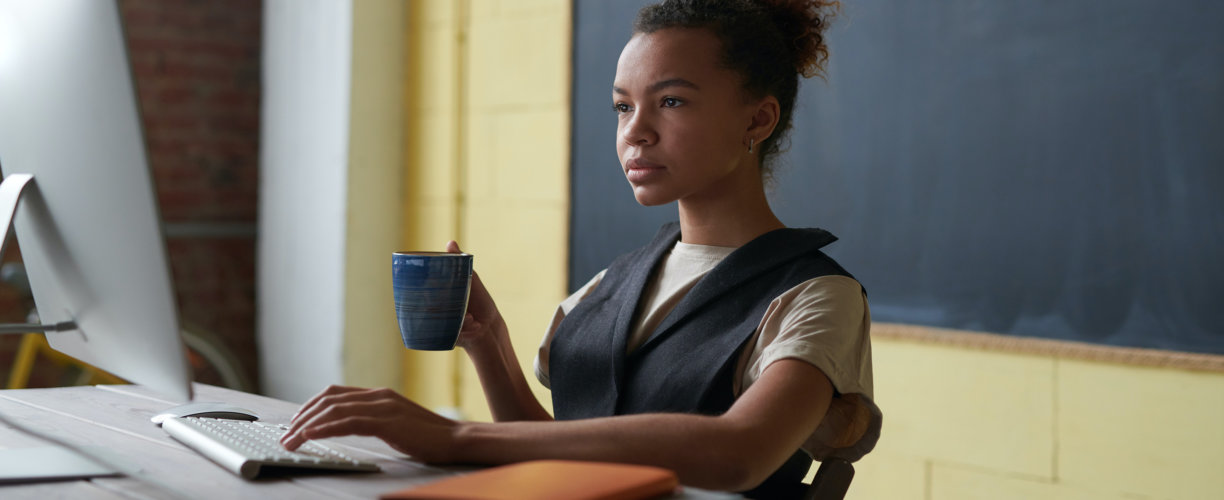 Student working on MAC holding a drink in a mug