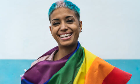 Person holding the LGBTQI+ flag with the trans flag colours in their hair