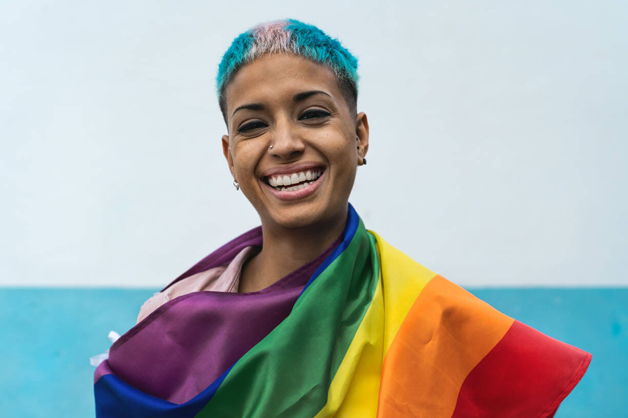 Person holding the LGBTQI+ flag with the trans flag colours in their hair