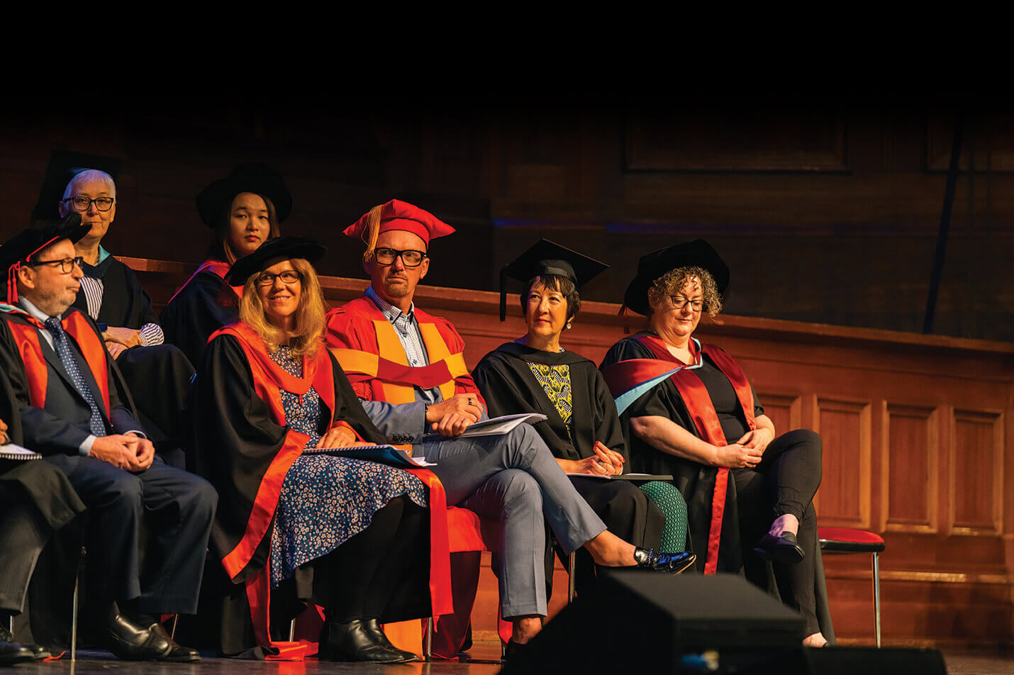 Faculty & Senior Staff Academic staff sit on stage in traditional and ceremonial robes and caps