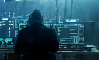 A programmer wearing a hoodie sitting in front of many laptops and computers