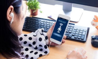 A female student holding a mobile phone listening to a podcast at her desk