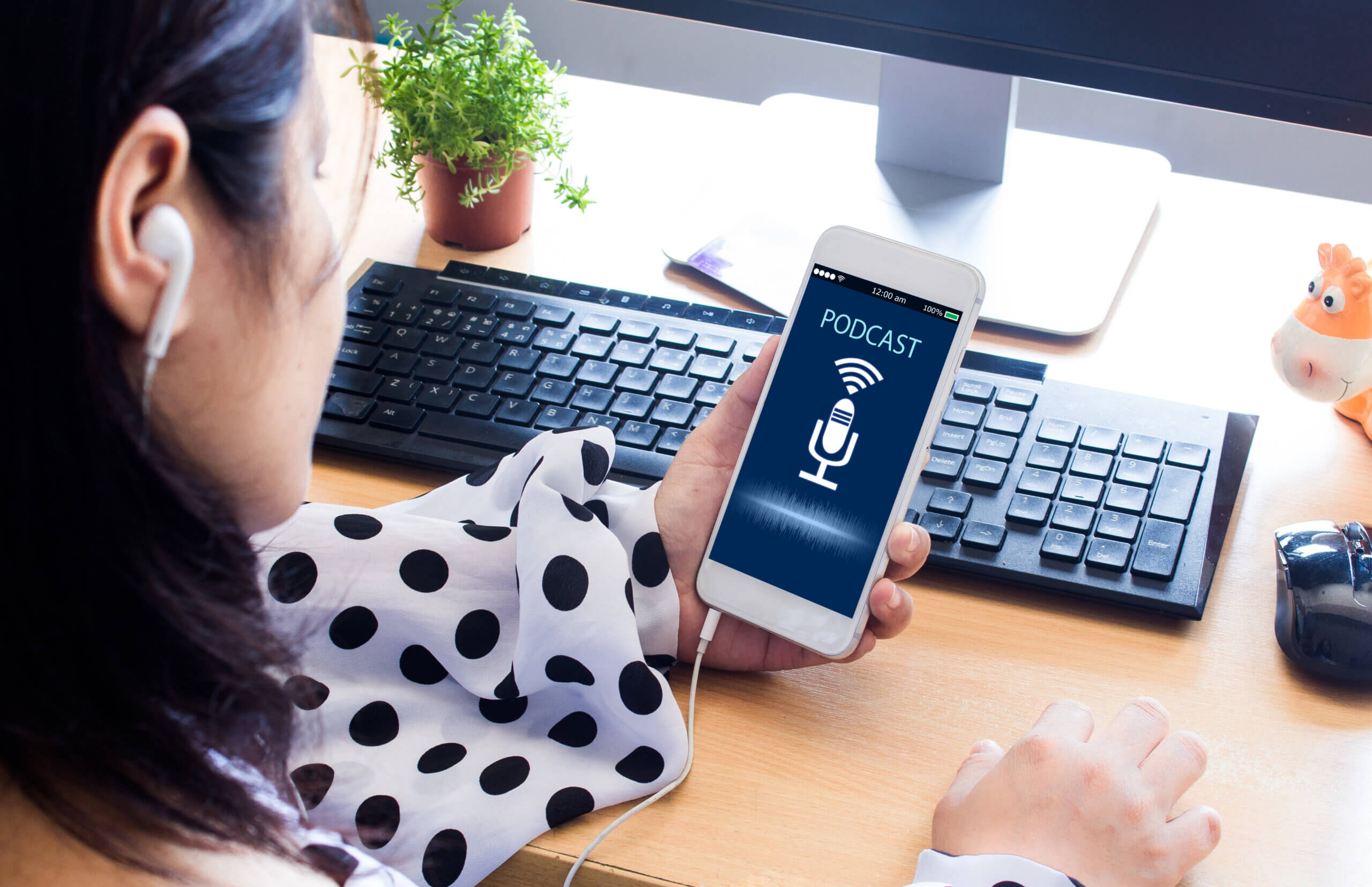 A female student holding a mobile phone listening to a podcast at her desk