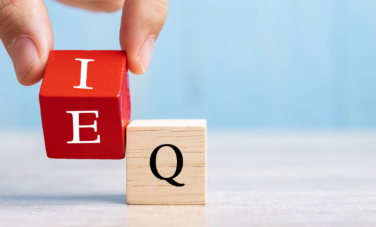 A hand holding two wooden blocks representing the letters E and Q for emotional intelligence