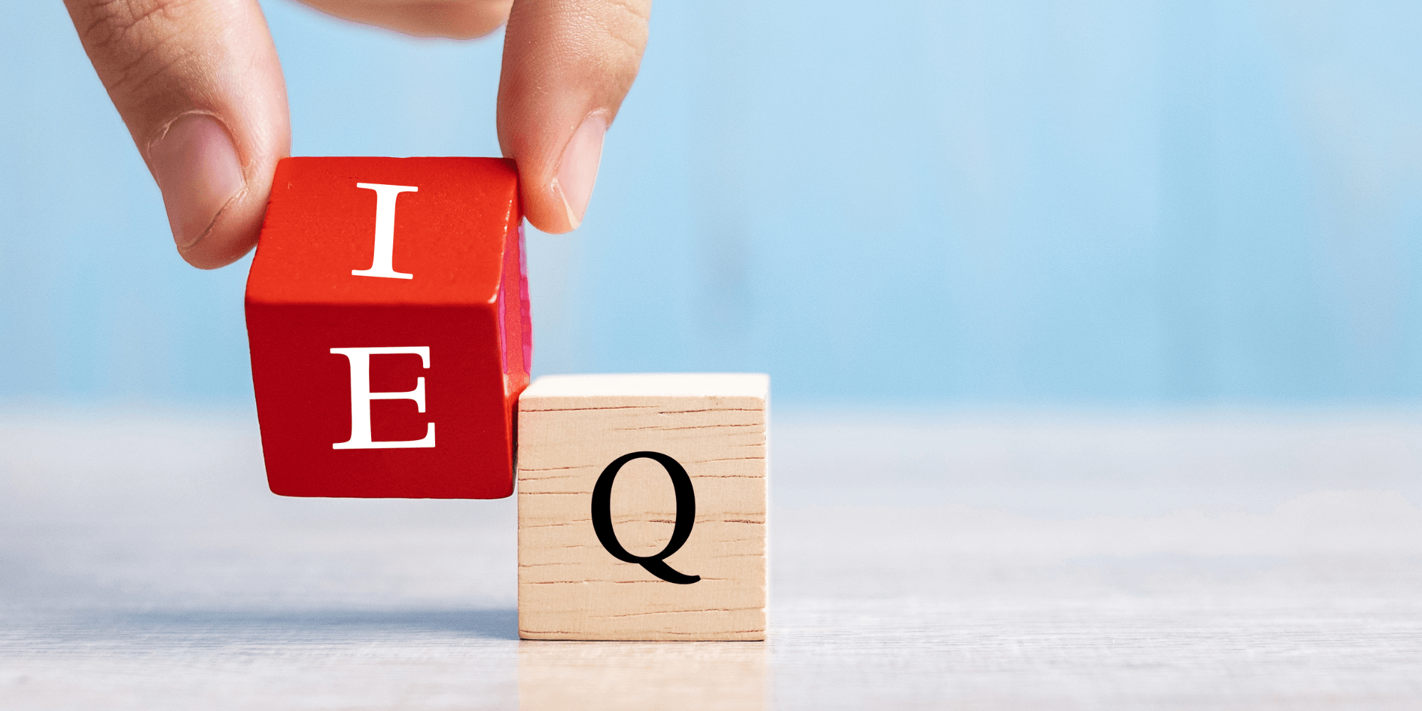 A hand holding two wooden blocks representing the letters E and Q for emotional intelligence