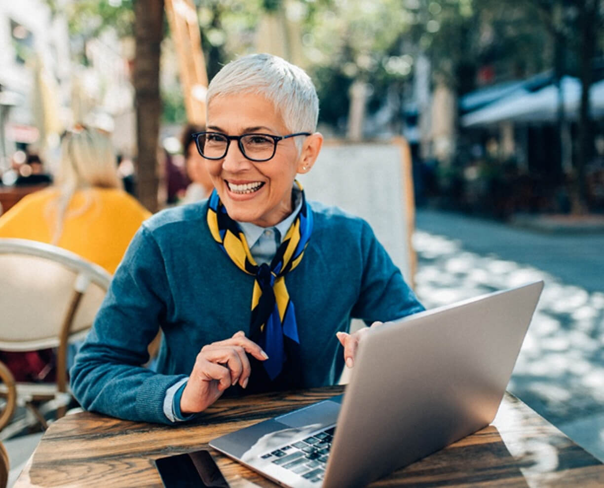 Woman with laptop at café Smiling woman using a laptop in an outdoor cafe ACAP Careers culture