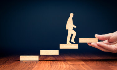 A wooden male figure climbing wooden block stairs to represent conquering life's challenges