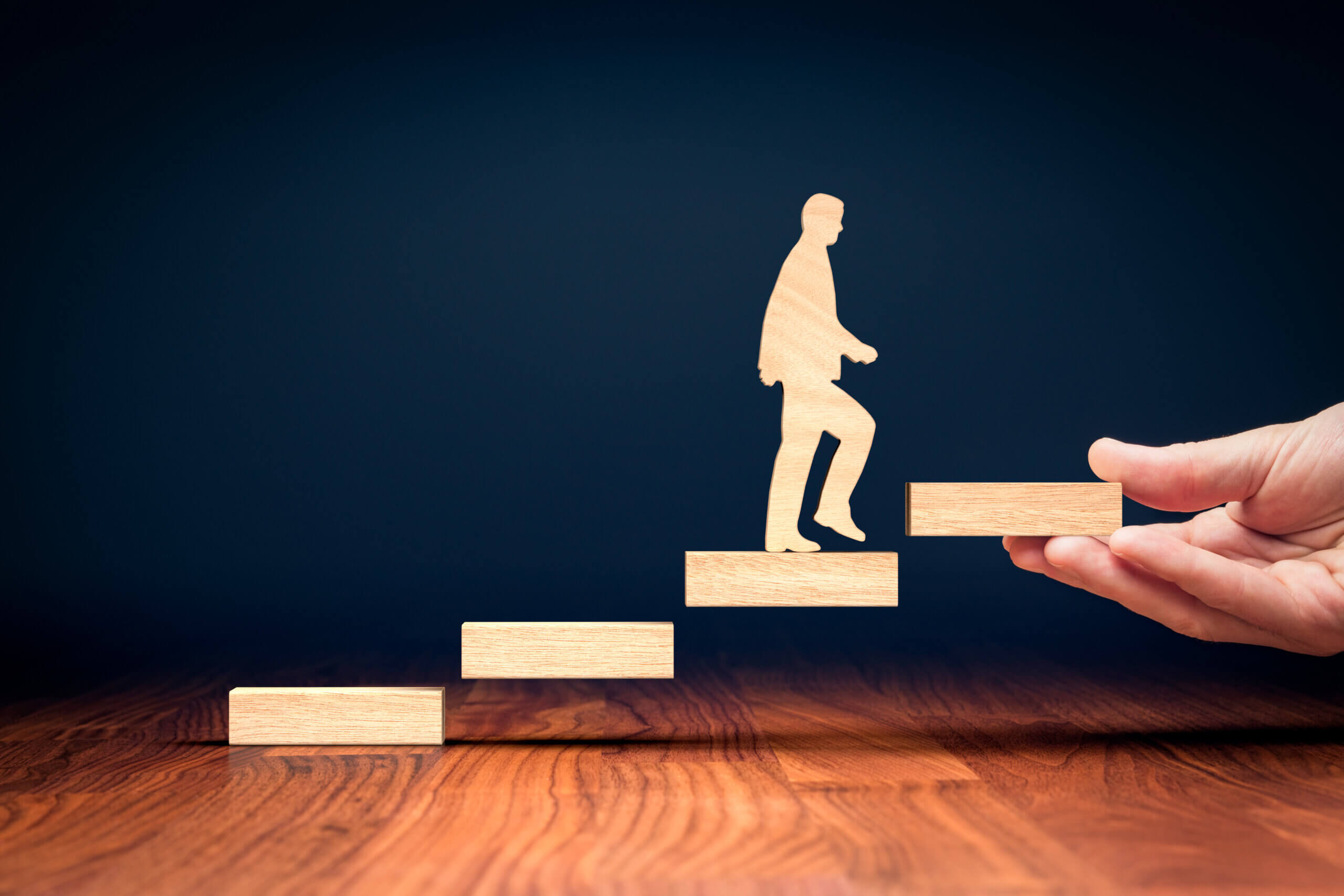 A wooden male figure climbing wooden block stairs to represent conquering life's challenges