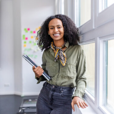 A young woman leaning against a window sill with notebooks in her hand ACAP Careers Academic Services