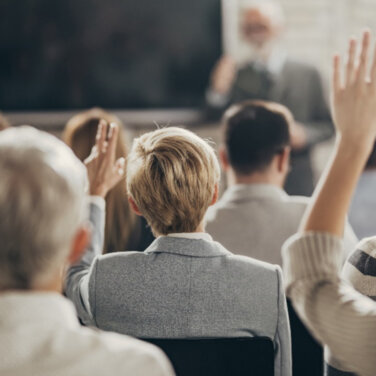 Rear view of a classroom with students holding their hands in the air ACAP Careers Law & Justice