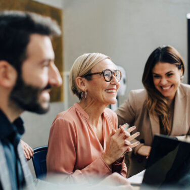 Two woman and two men smiling, working together on laptops in a classroom ACAP Careers MBA, coaching and IT