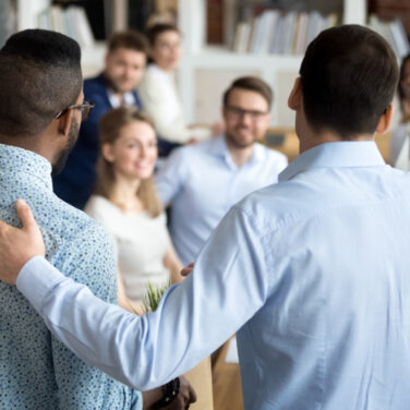 One man with his hand on the shoulder of another man standing in front of a class group ACAP Careers Student Engagement