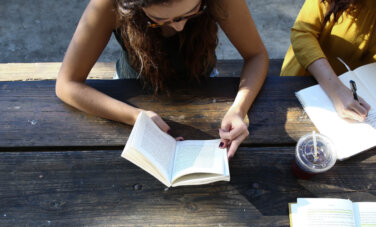 Students outside on a picnic table, reading and writing in books