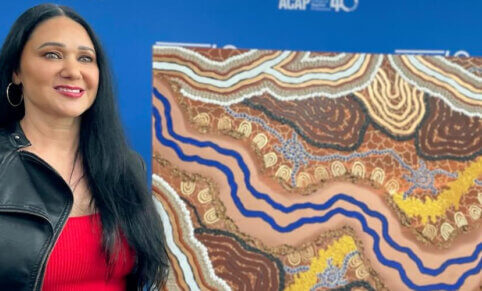 Simone Thomson standing in front of Indigenous artwork