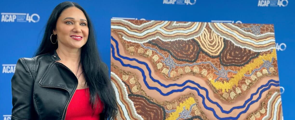 Simone Thomson standing in front of Indigenous artwork