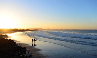 Destination Australia hero image desktop Two people walking along a beach in Byron Bay at sunrise