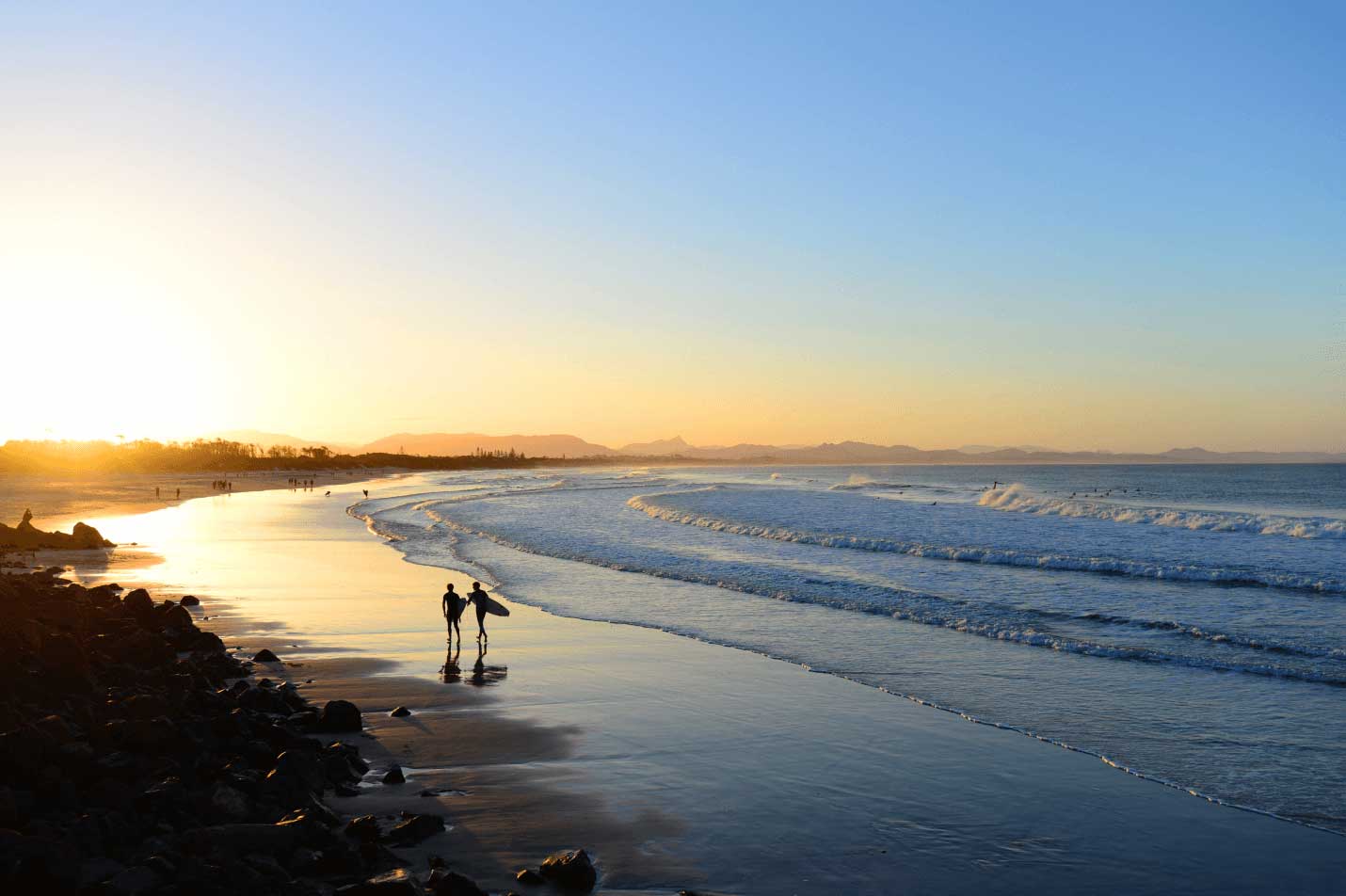 Two people walking along a beach in Byron Bay at sunrise