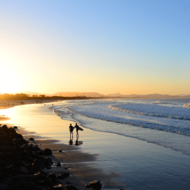 Two people walking along a beach in Byron Bay at sunrise