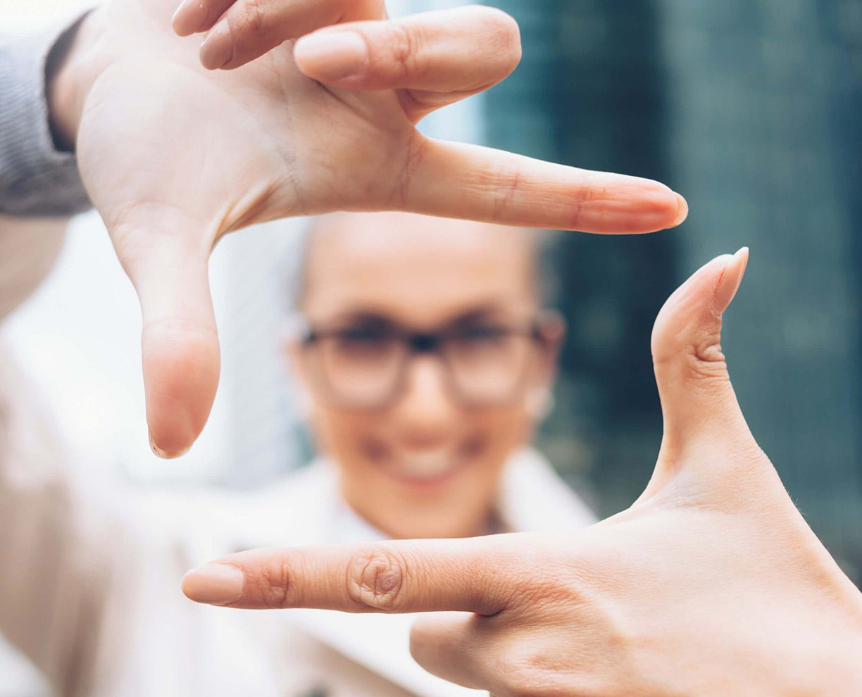 Course-overview-woman-hand-frame A woman's hands creating a frame with her thumb and index finger, with her face showing through the frame in the background - out of focus.