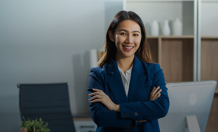 A woman in a dark blue suit folding her arms and smiling towards camera - ACAP Graduate Diploma of Professional Accounting (828x676)