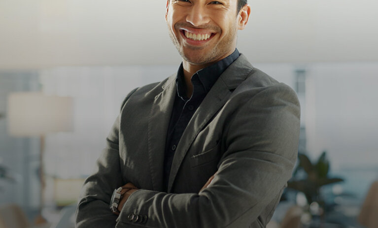 A man in a green and black shirt standing in an office with his arms folded, smiling towards camera - ACAP Master of Professional Accounting (2880x1188)