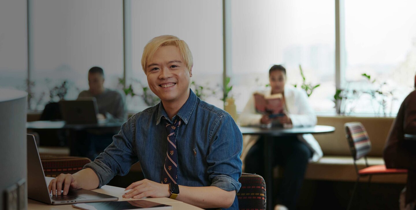 ACAP Psychology student Tidus sitting with a laptop on an ACAP University College campus and smiling towards camera (1430x952)