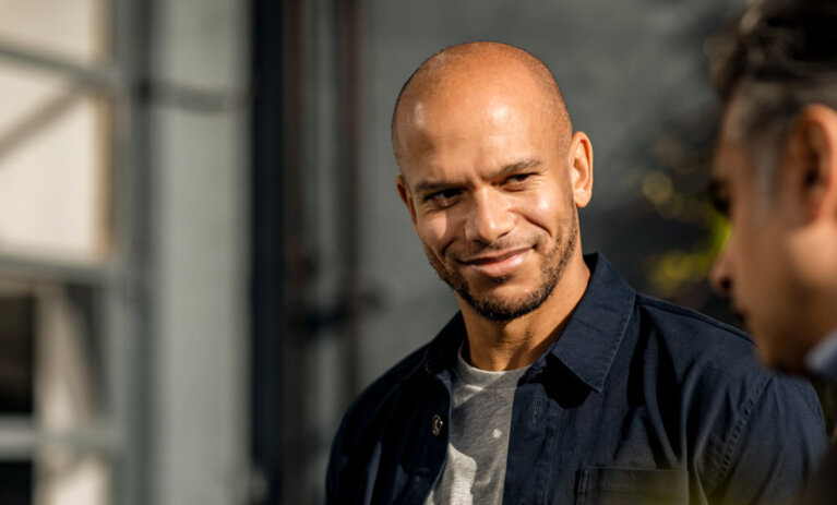 Man smiles at another man in foreground.