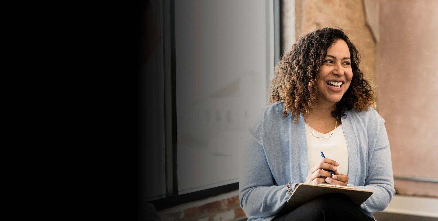 Smiling woman sitting and holding a pen and clipboard