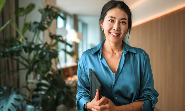 Smiling woman standing and looking towards the camera with a tablet under her arm