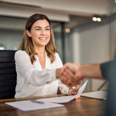 Young smiling woman sitting, shaking someone's hand over a work desk