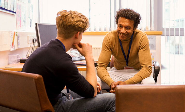 Smiling man sitting at a desk and chairs, meeting with a young client