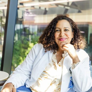 Smiling woman sitting on a chair, resting her chin on her hand and looking towards the camera