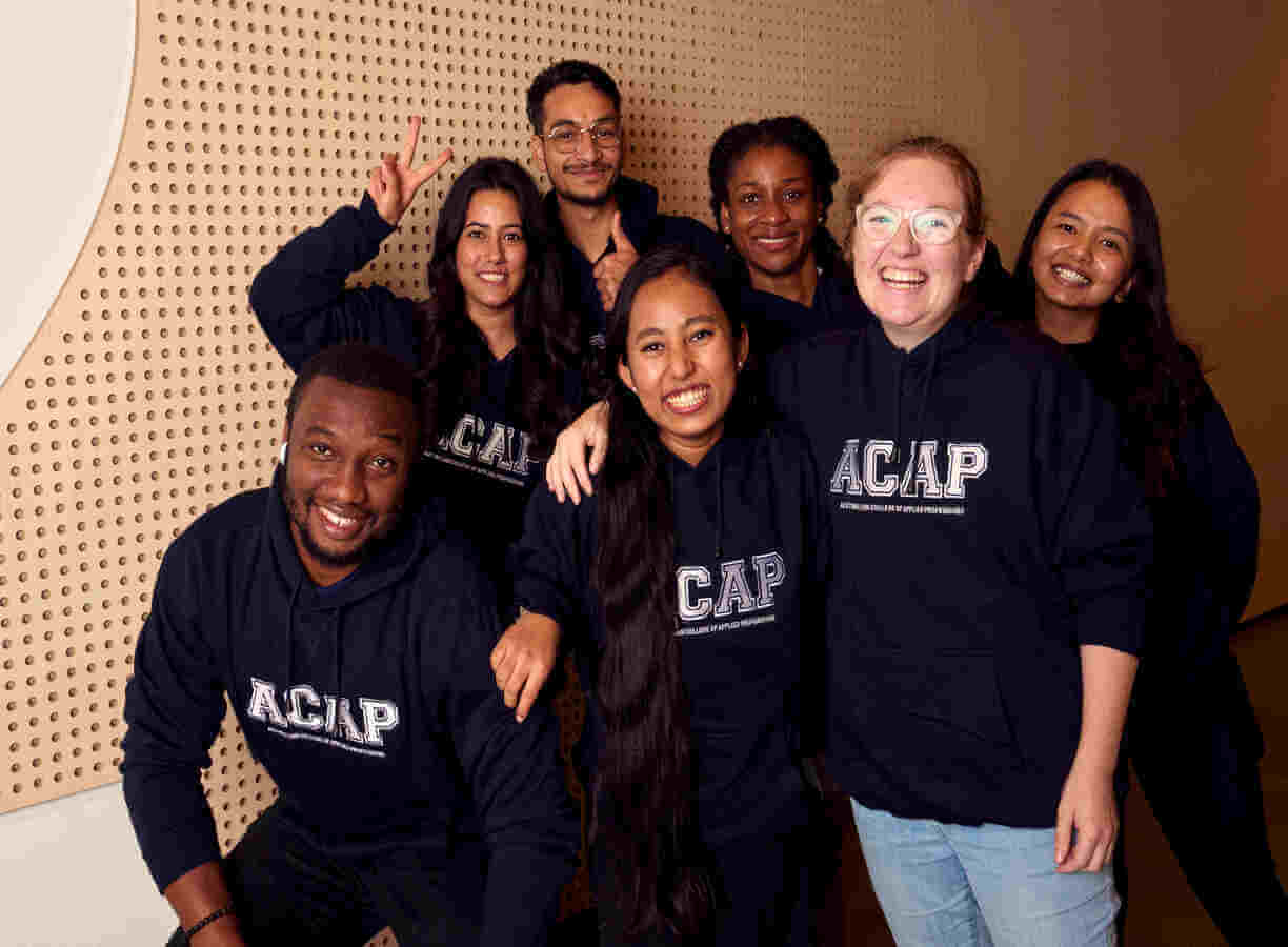 Seven student in ACAP hoodies, standing in a huddle and smiling to camera