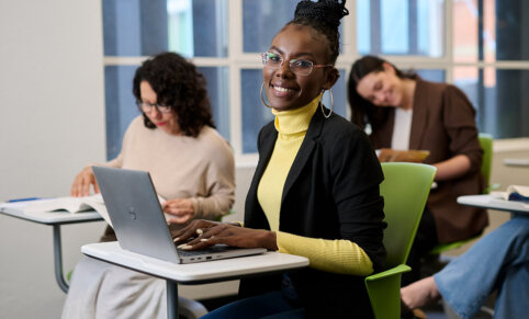 A female student sitting on a green chair and working on a desk with a laptop at ACAP University College Adelaide campus - 1224x990